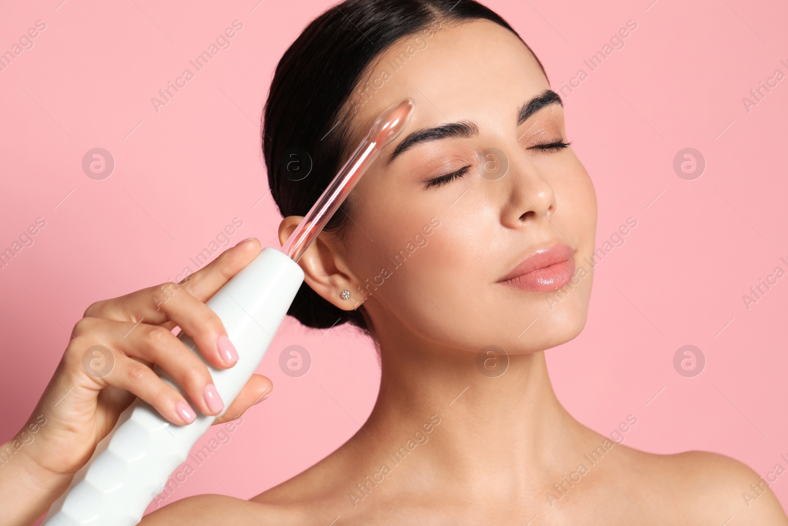 Photo of Woman using high frequency darsonval device on pink background