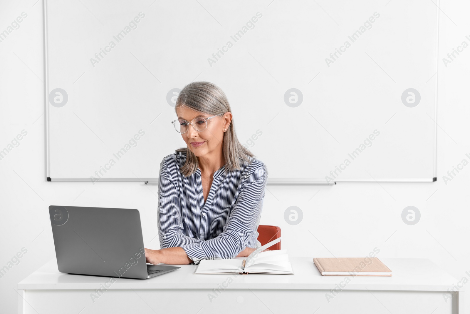 Photo of Professor giving lecture while using laptop at desk in classroom, space for text