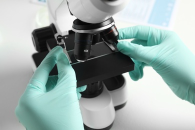 Medical assistant using modern microscope at white table, closeup