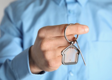 Young man holding house key with trinket, closeup