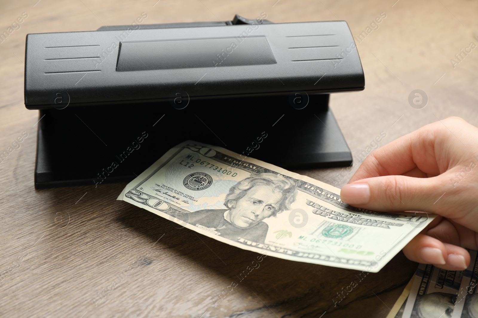 Photo of Woman checking dollar banknote with currency detector at wooden table, closeup. Money examination device