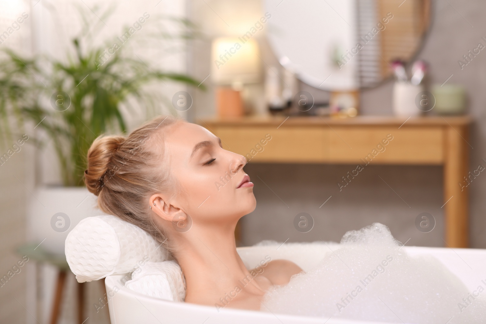 Photo of Young woman using pillow while enjoying bubble bath indoors