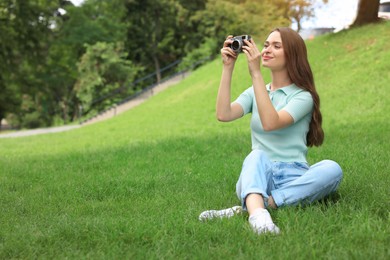Young woman with camera taking photo on green grass outdoors, space for text. Interesting hobby