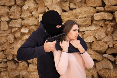 Masked man with gun holding woman hostage  outdoors. Criminal offence