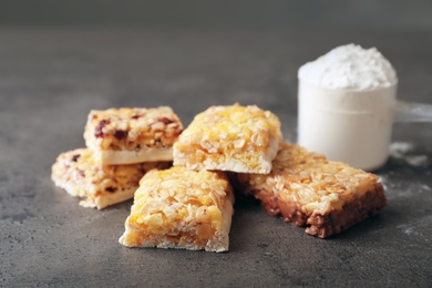 Photo of Tasty protein bars and scoop of powder on grey table