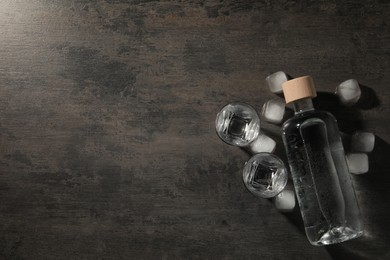Photo of Bottle of vodka and shot glasses with ice on black table, flat lay. Space for text