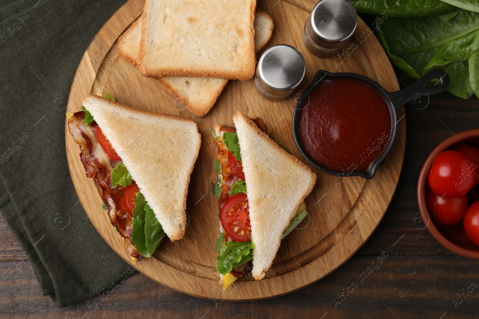 Photo of Delicious sandwiches with fried bacon, ketchup and spices on wooden table, flat lay