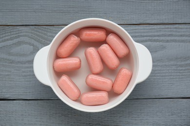 Photo of Bowl of delicious sausages on grey wooden table, top view