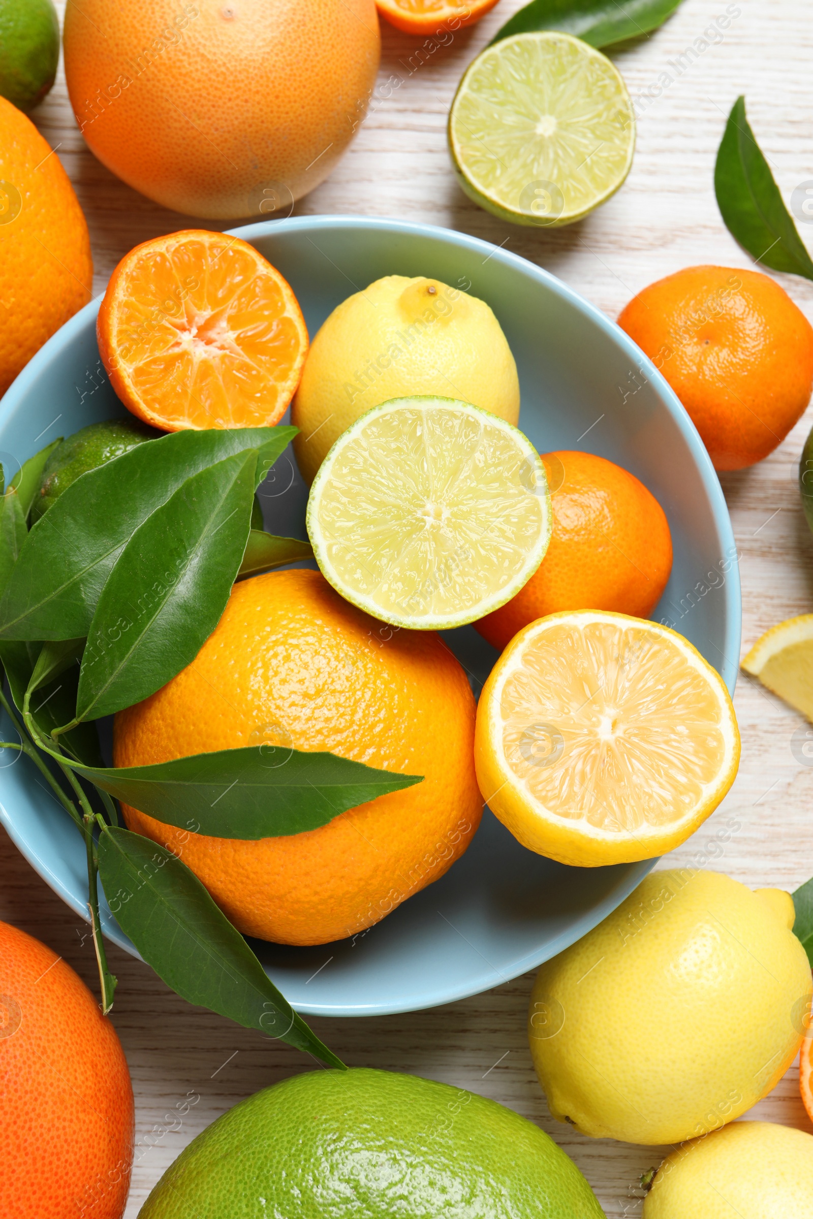 Photo of Different ripe citrus fruits with green leaves on white wooden table, flat lay