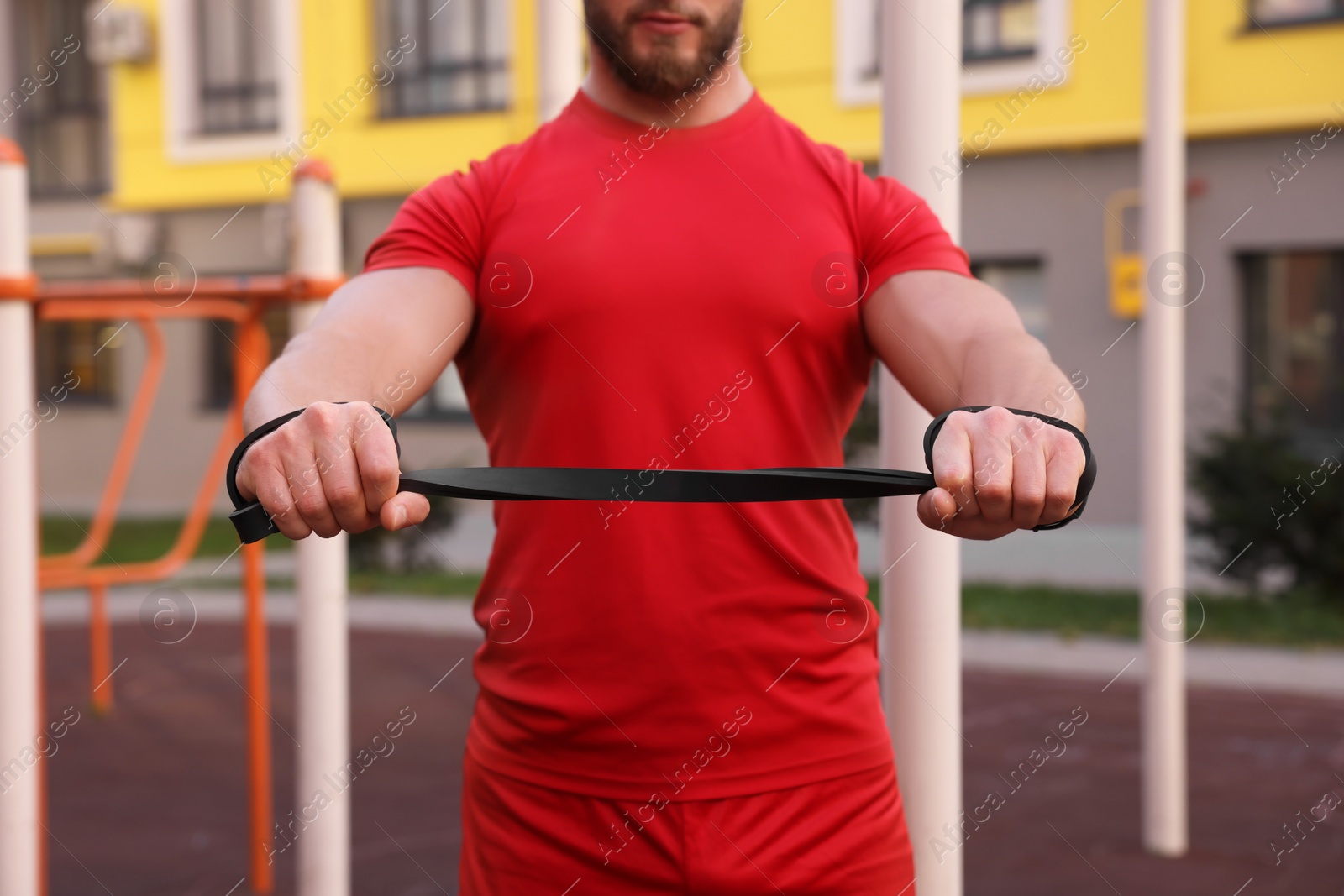 Photo of Muscular man doing exercise with elastic resistance band outdoors, closeup