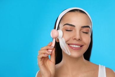 Young woman using facial cleansing brush on light blue background. Washing accessory