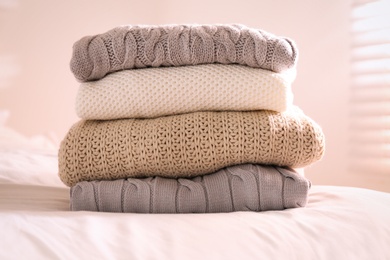 Stack of folded warm sweaters on bed indoors