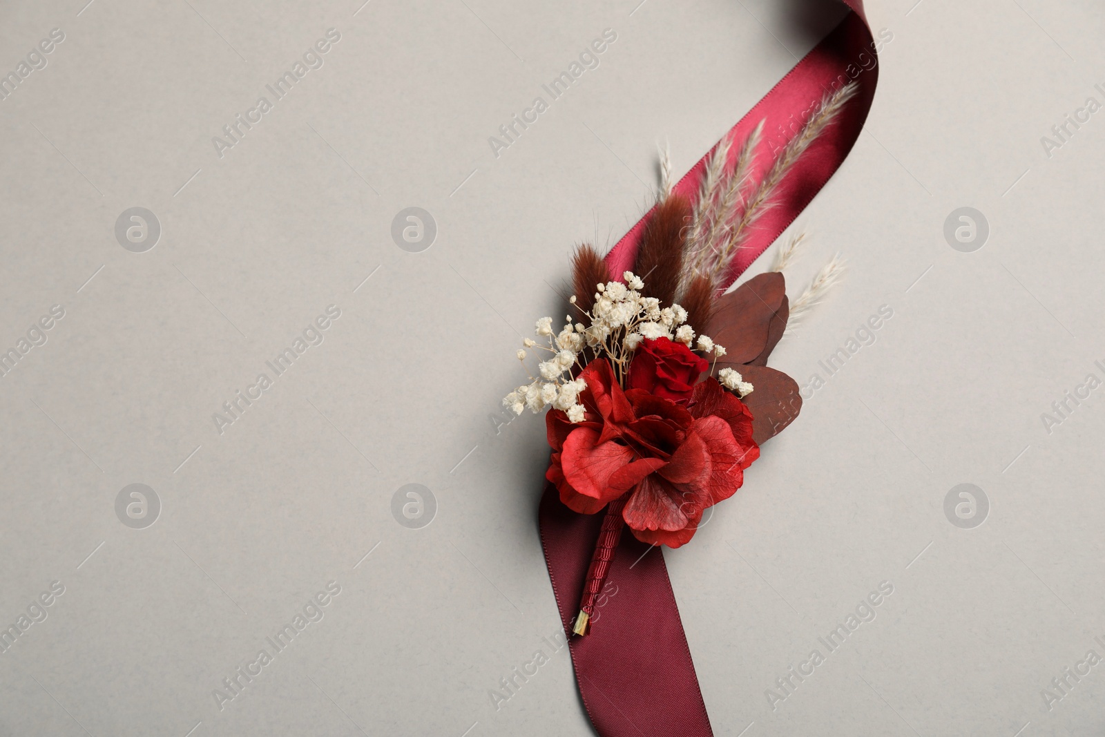 Photo of Stylish boutonniere and red ribbon on light grey background, top view. Space for text