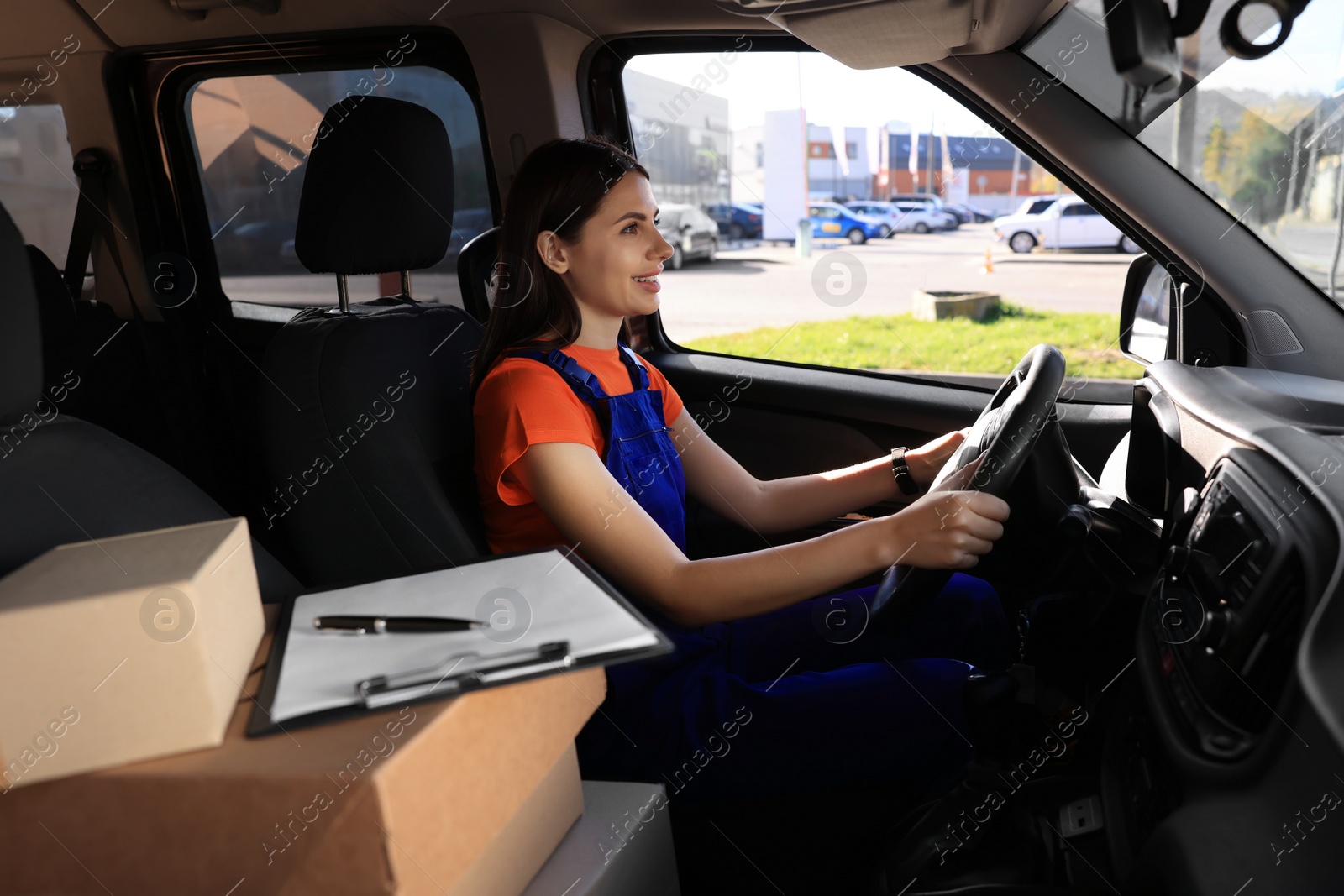 Photo of Courier with clipboard and parcels in car. Delivery service