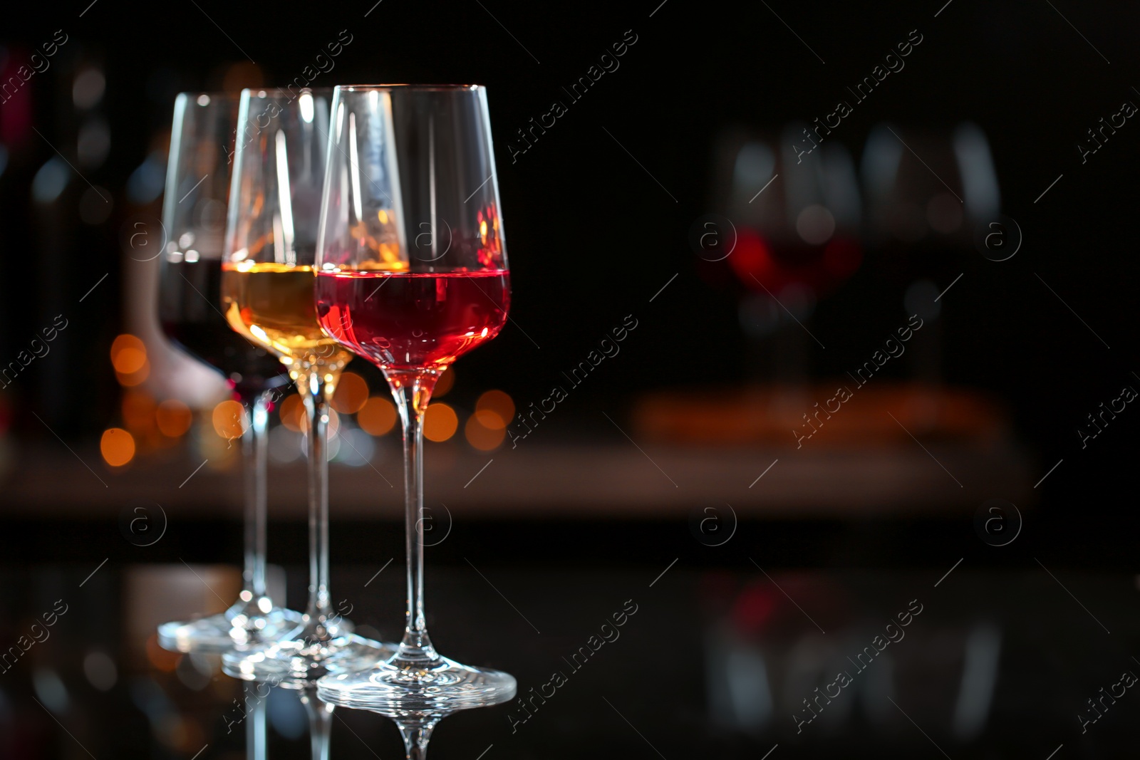 Photo of Row of glasses with different wines on bar counter against blurred background. Space for text