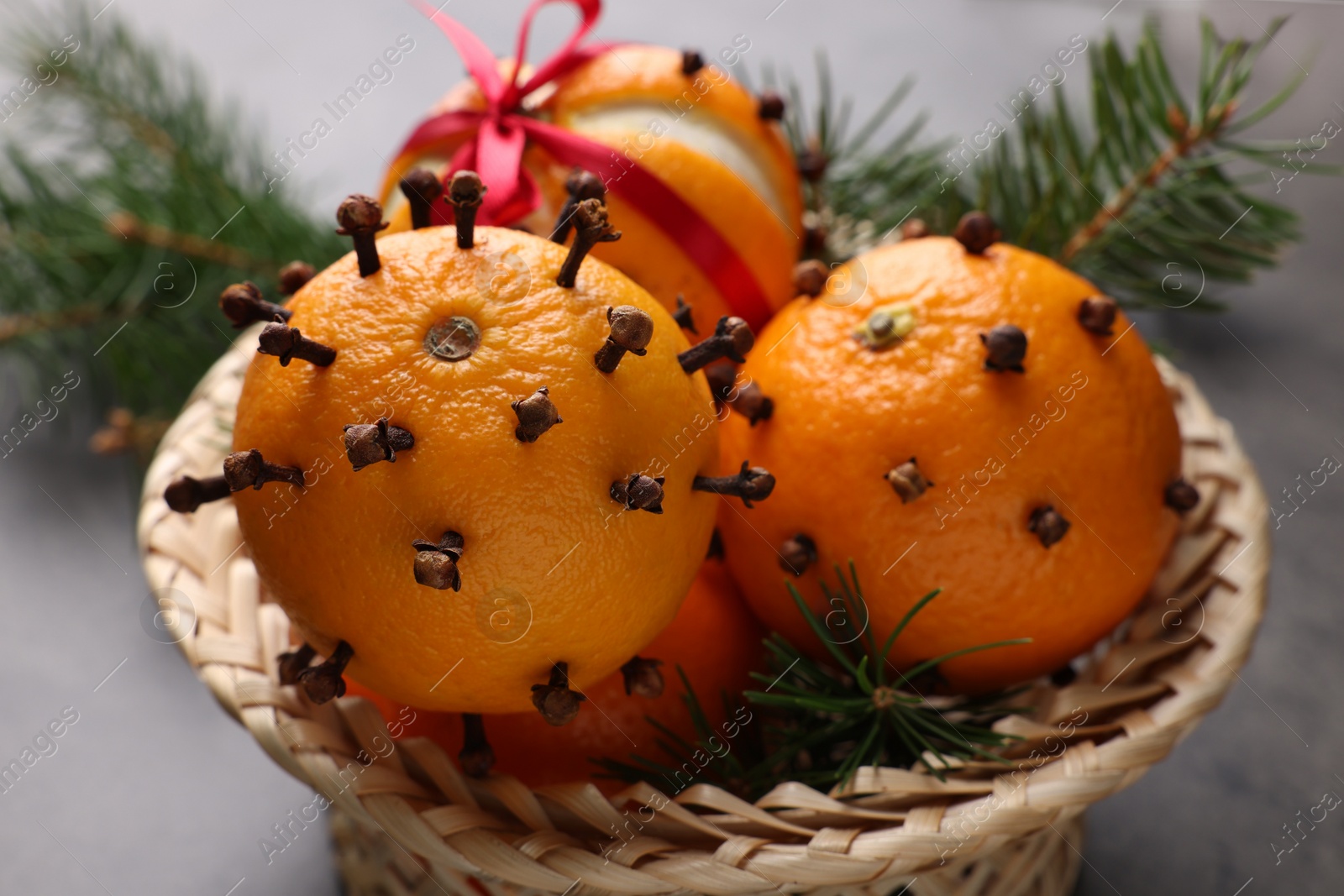 Photo of Pomander balls made of tangerines with cloves and fir branches on grey table, closeup