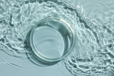 Photo of Stylish presentation for product. Glass podium in water on light blue background, top view