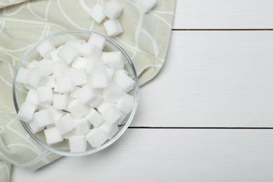 Many sugar cubes in glass bowl on white wooden table, top view. Space for text