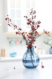 Photo of Hawthorn branches with red berries on table in kitchen