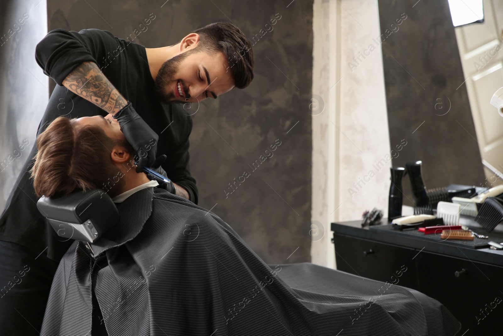 Photo of Professional hairdresser shaving client with straight razor in barbershop