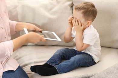 Photo of Internet addiction. Mother taking away tablet from her little son on sofa at home, closeup