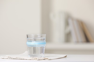 Photo of Glass of pure water and napkin on white table indoors. Space for text