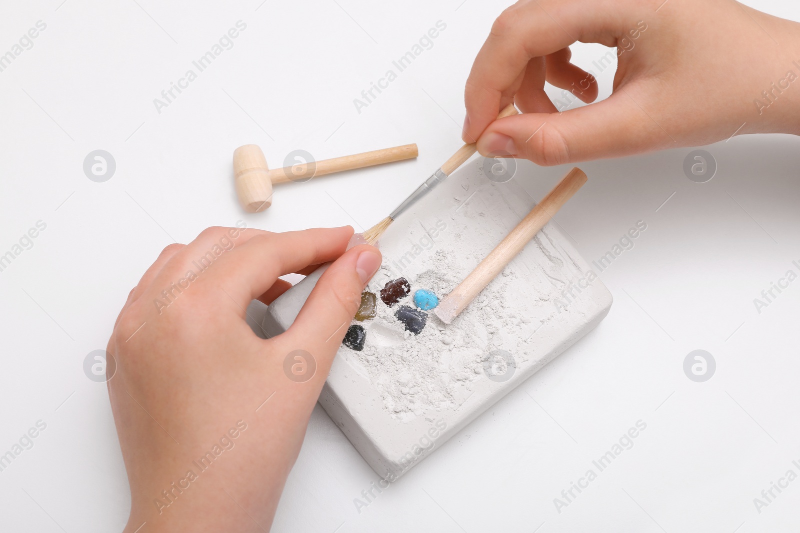 Photo of Child playing with Excavation kit at white table, above view. Educational toy for motor skills