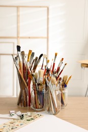 Photo of Different brushes, paints and palette on wooden table indoors. Artist's workplace