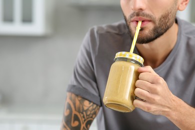 Photo of Man drinking delicious smoothie in kitchen, closeup. Space for text