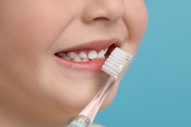 Photo of Cute little boy brushing his teeth with electric toothbrush on light blue background, closeup. Space for text
