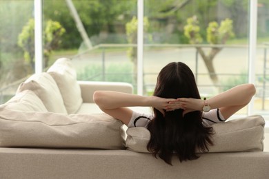 Teenage girl relaxing on sofa at home, back view