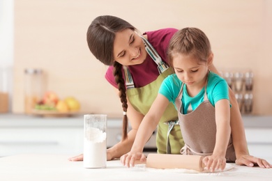 Photo of Mother and her daughter preparing dough at table in kitchen