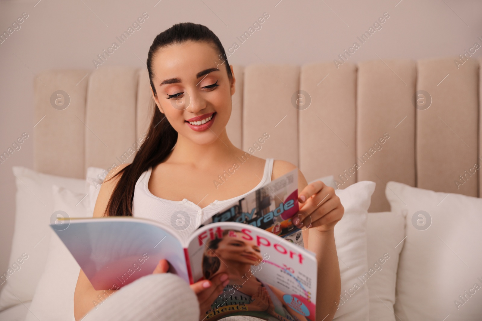 Photo of Happy woman reading magazine on bed indoors