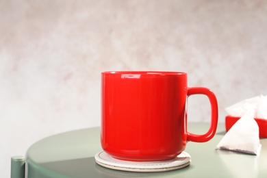 Photo of Cup and pyramid teabag on table against color background