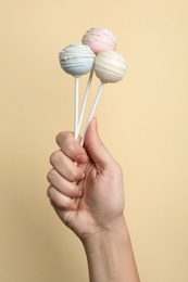 Photo of Woman holding sweet cake pops on light background, closeup