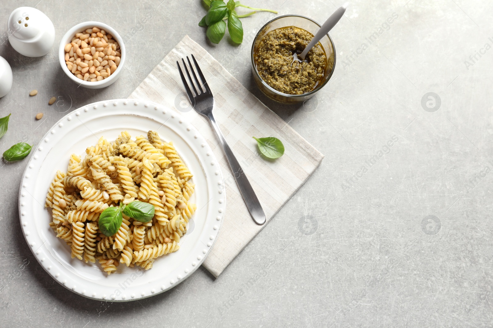 Photo of Flat lay composition with plate of delicious basil pesto pasta and space for text on gray table