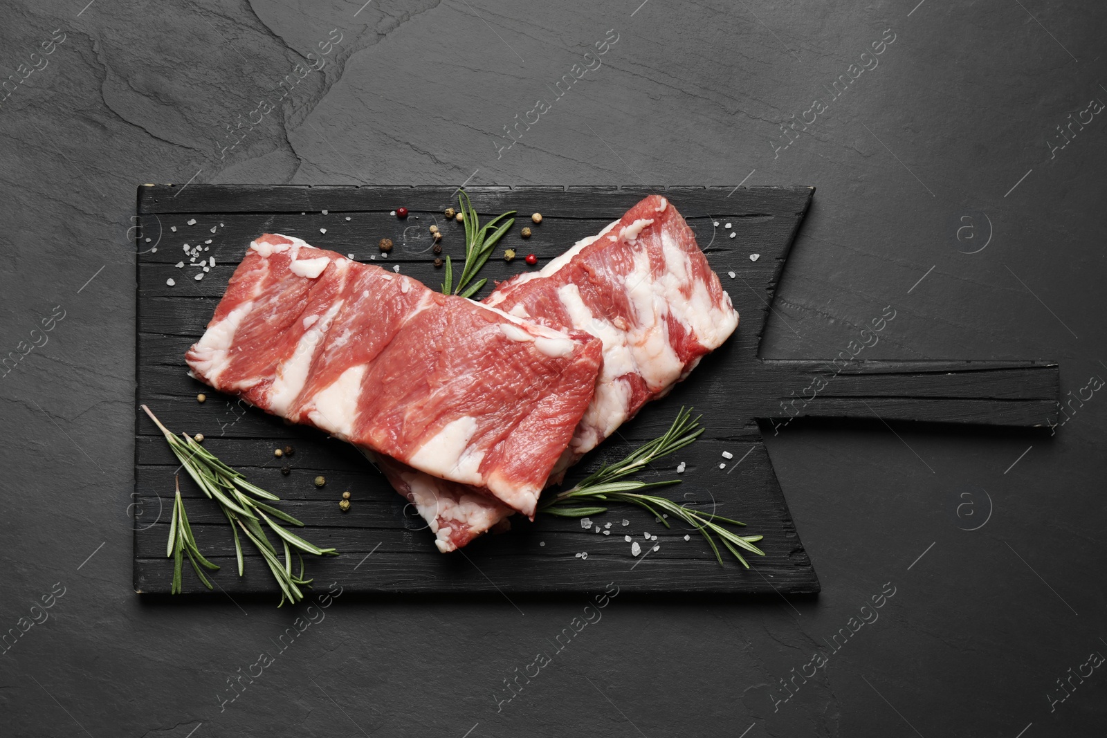 Photo of Raw ribs with rosemary and spices on black table, top view