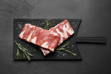 Raw ribs with rosemary and spices on black table, top view