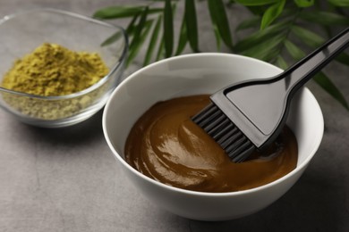 Photo of Bowl of henna cream and brush on light grey table, closeup. Natural hair coloring