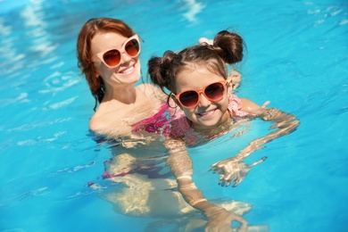 Photo of Young woman teaching her daughter to swim in pool