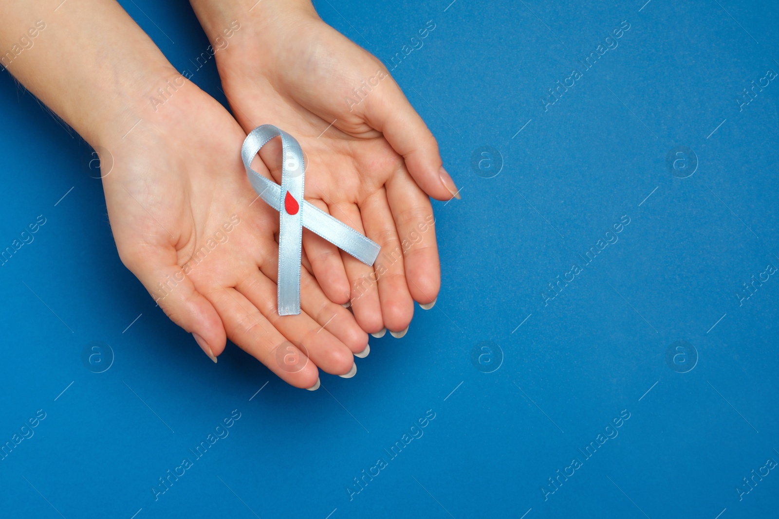 Photo of Woman holding light blue ribbon with paper blood drop on color background, top view and space for text. Diabetes awareness