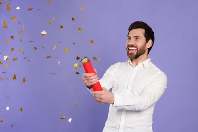 Photo of Happy man blowing up party popper on violet background