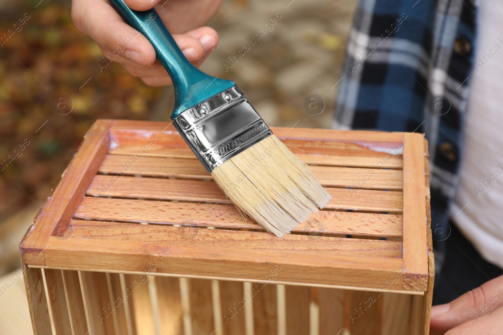 Photo of Man applying varnish onto wooden crate against blurred background, closeup