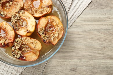 Photo of Delicious baked quinces with nuts and honey in bowl on wooden table, top view. Space for text