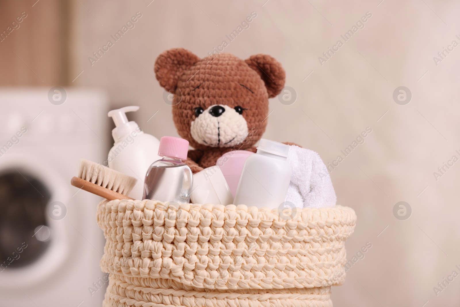 Photo of Baby cosmetic products, bath accessories and toy bear in knitted basket indoors, closeup