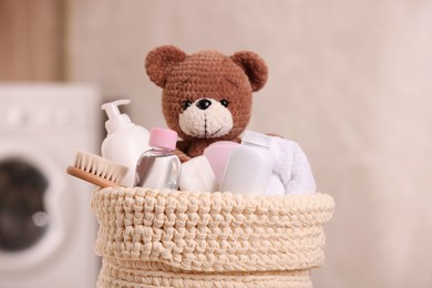 Baby cosmetic products, bath accessories and toy bear in knitted basket indoors, closeup