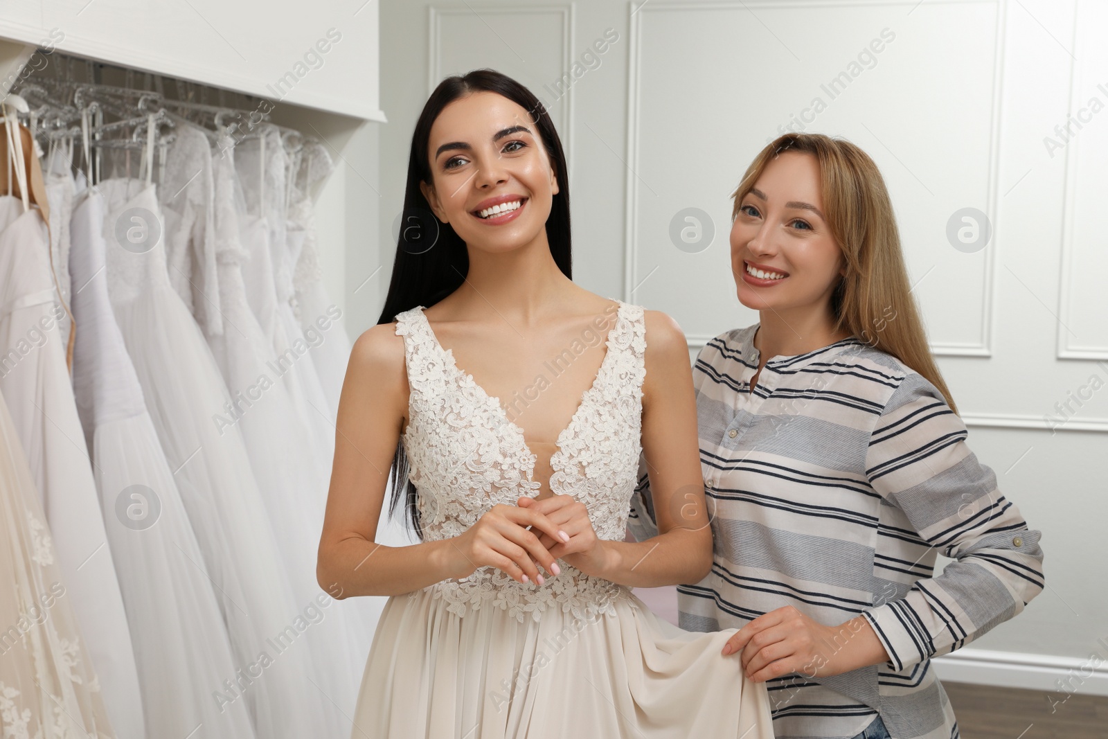 Photo of Woman helping bride wear wedding dress in boutique