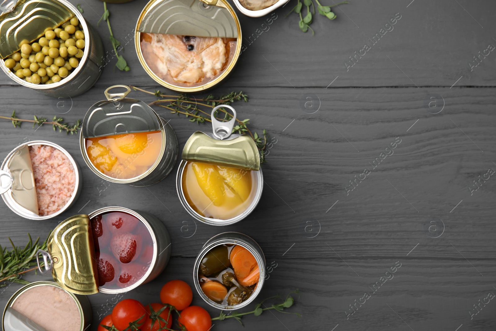 Photo of Open tin cans with different products on gray wooden table, flat lay. Space for text