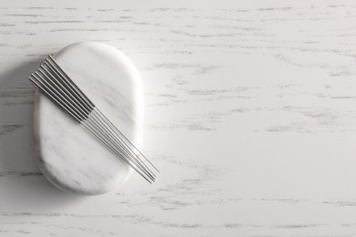 Acupuncture needles and spa stone on white wooden table, top view. Space for text