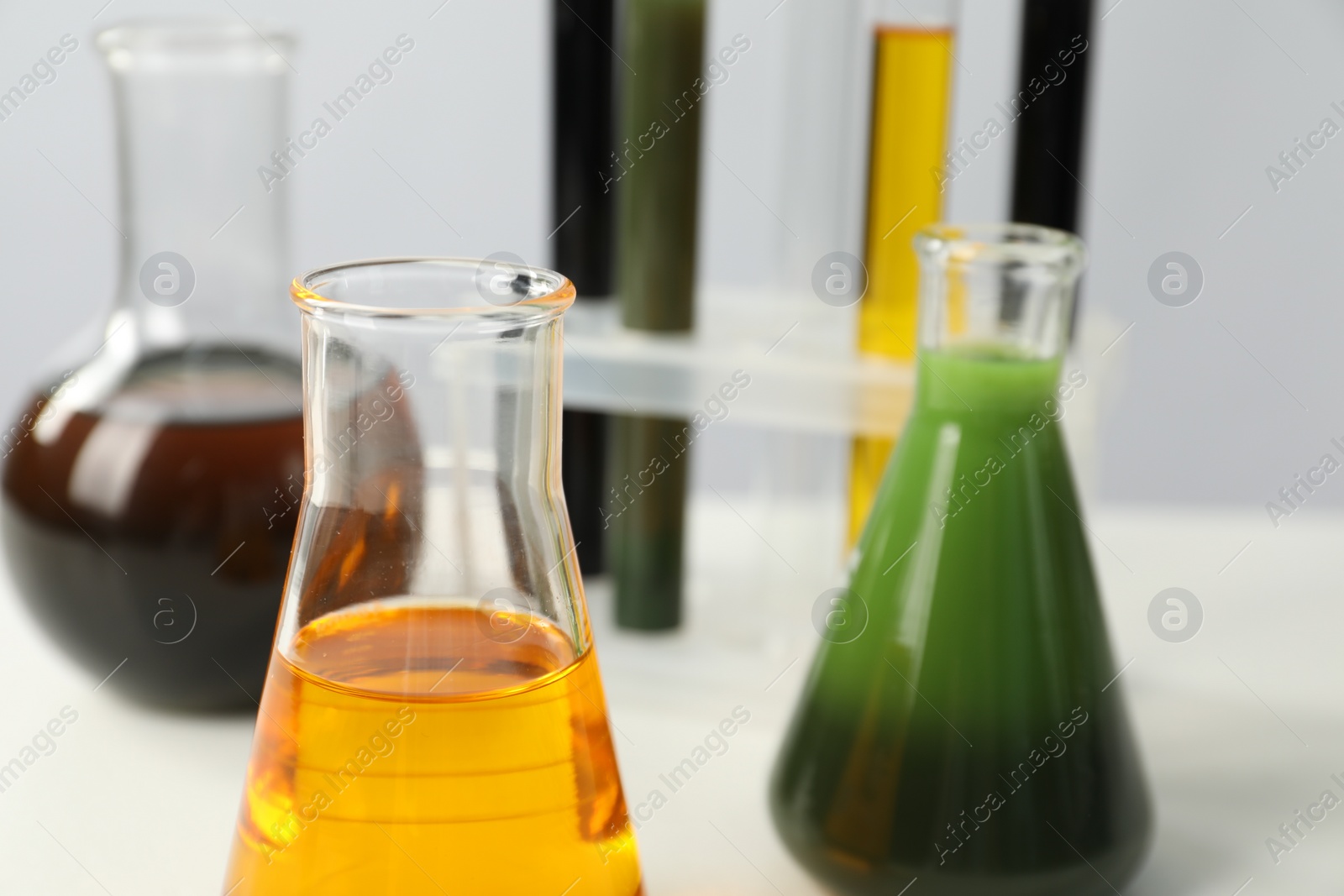 Photo of Laboratory glassware with different types of oil on white table, closeup